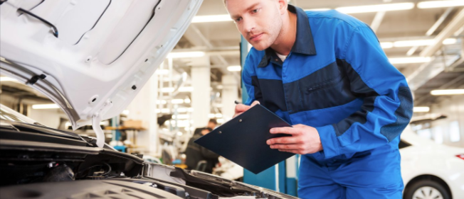 Auto repair customer checking vehicle details and recording information on a service inspection form beside a car with its bonnet open.