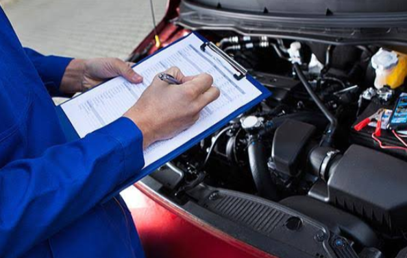 Mechanic writing on a clipboard beside an open car hood while planning appointment recovery at an auto repair shop